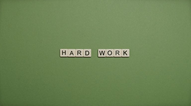 Tiles spelling 'hard work' on a green background symbolizing diligence and effort.